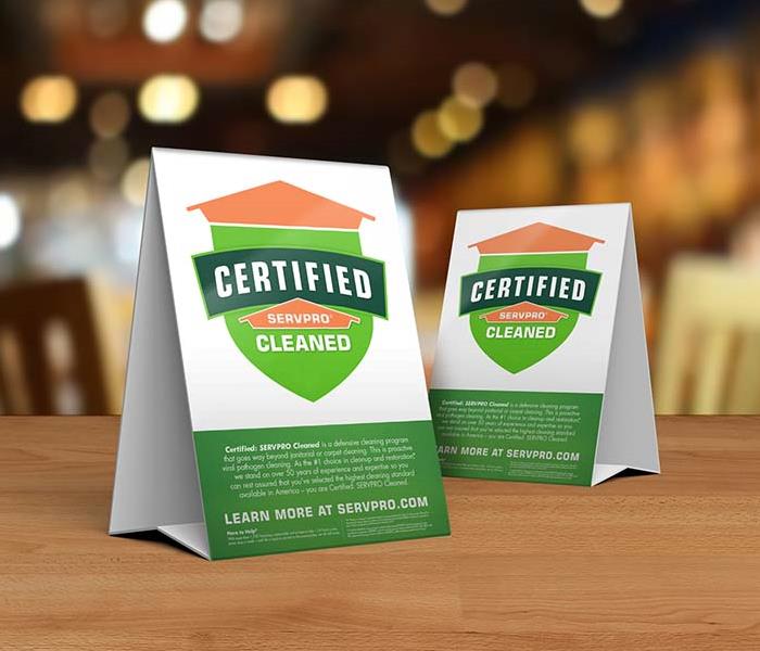 Table tent signs describing the Certified: SERVPRO Cleaned program on top of a wooden table